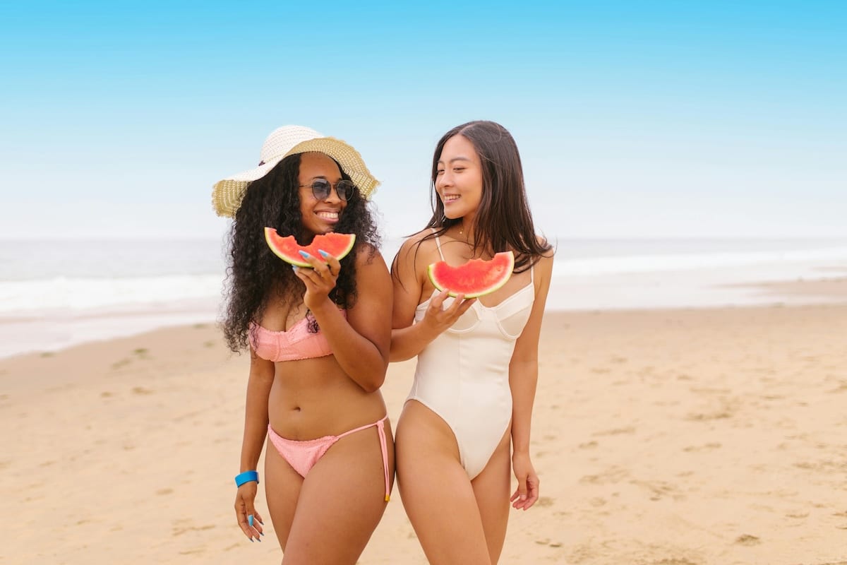 2 Freundinnen haben Spaß im Sommer am Strand und essen leckere Wassermelone