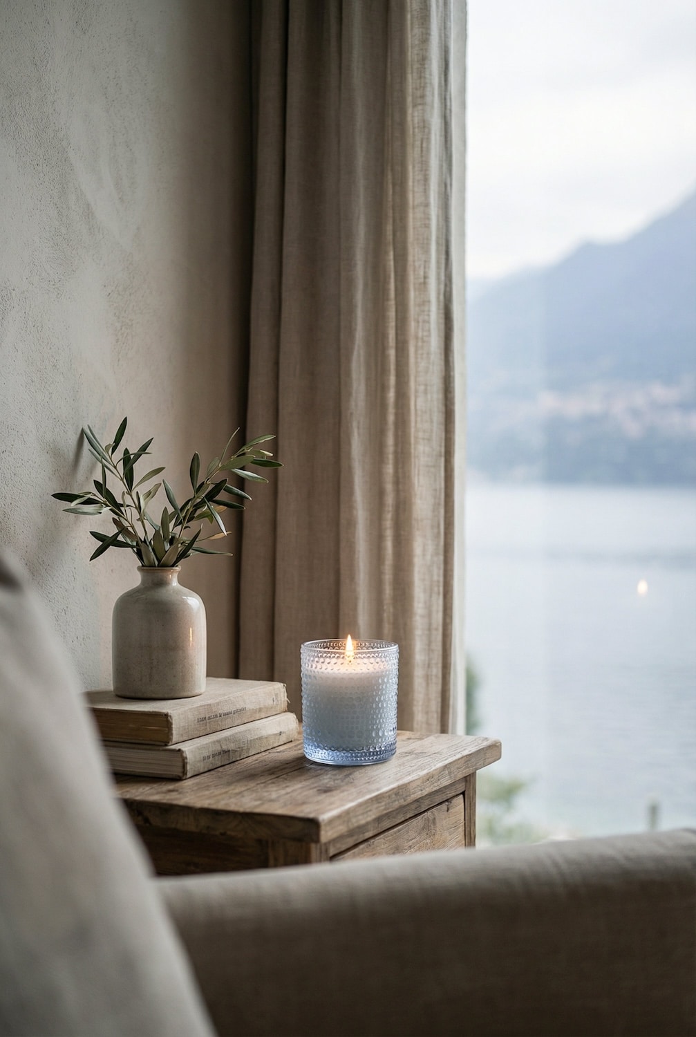 Lake Garda Duftkerze von AVA & MAY auf Holzkommode am Fenster mit Seeblick – frischer Raumduft aus Grünem Tee, Gurke und Maiglöckchen.